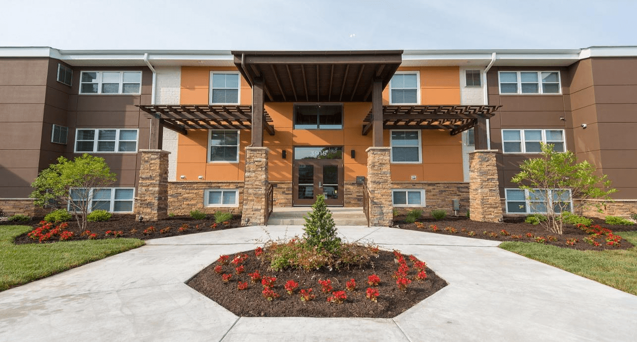 A building with a brown and orange facade has a large front entrance with a flower bed in front.